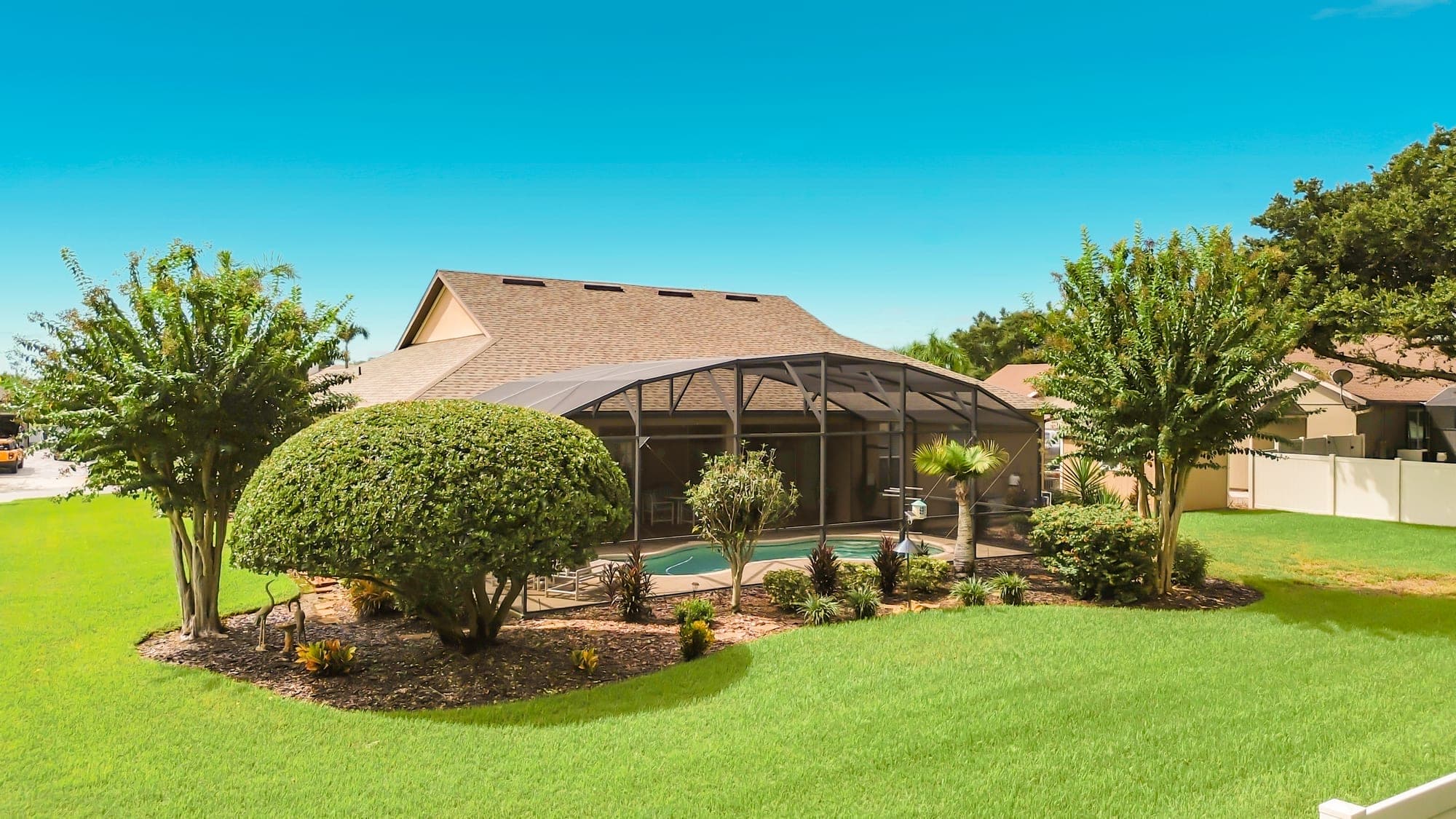 Back yard at 5243 Hammock Pointe Ct — landscaped beds and crape myrtles around the pool enclosure